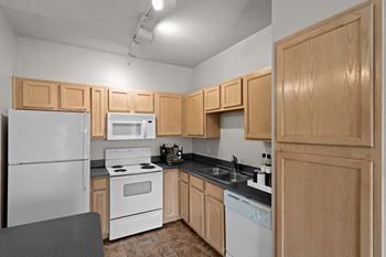 A kitchen with white all-electric appliances including microwave & dishwasher, oak cabinetry, and track lighting.